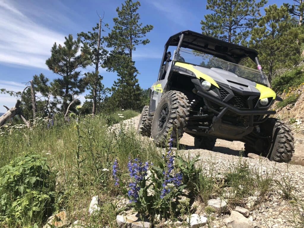 2-seater Yamaha UTV driving around corner on trail surrounded by pine trees in the black hills